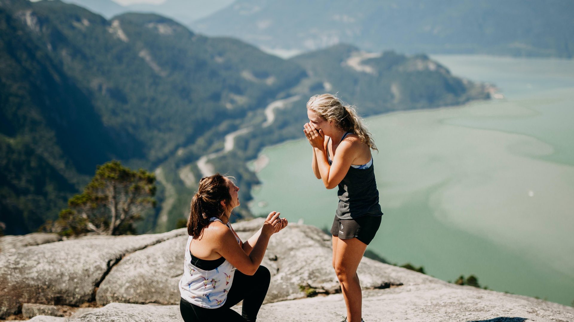Woman on one knee proposing to another woman. Stood in front of mountain landscape on Valentine's Day